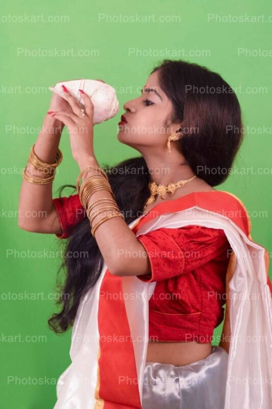 DG14923660922, traditional hindu girl blowing shankha stock image, stock photos, hindu stock photos, traditional stock photos, bengali woman stock photos, agomoni photoshoot, puja photoshoot, girl, indian girl, indian cute girl, ma, culture, south asian culture, bengal, clay, clay idol, celebration, puja, festival, indian girl images, bengali festival, celebration, asia, bengali, festival costume, devi, beauty, face, clothing, ceremony, bridal, jewellery, durga model, festival season, durga puja look. girl with sari, sari, tradition, bengali tradition, god, durga puja look photo shoot with white and red saree, bengali saree, female, glamor, ethnicity, women, model, culture model, durga puja model, durga puja model hd image, puja model pose, festival model photoshoot, festival model images, lady, indian girl photoshoot, green background photoshoot, gorgeous, hindu girl, hindu girl photoshoot, stock, royaly, new, shankha, blowing shankha, shankha model stock phtos