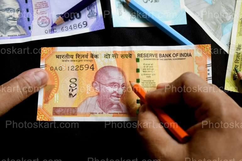 One Two Hundred Rupee Note Holding A Pen Image